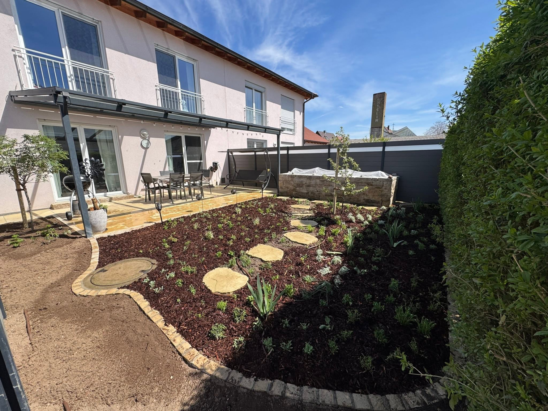 Neu angelegte Terrasse mit Natursteinbelag und frisch bepflanztem Beet im Raum Nördlingen