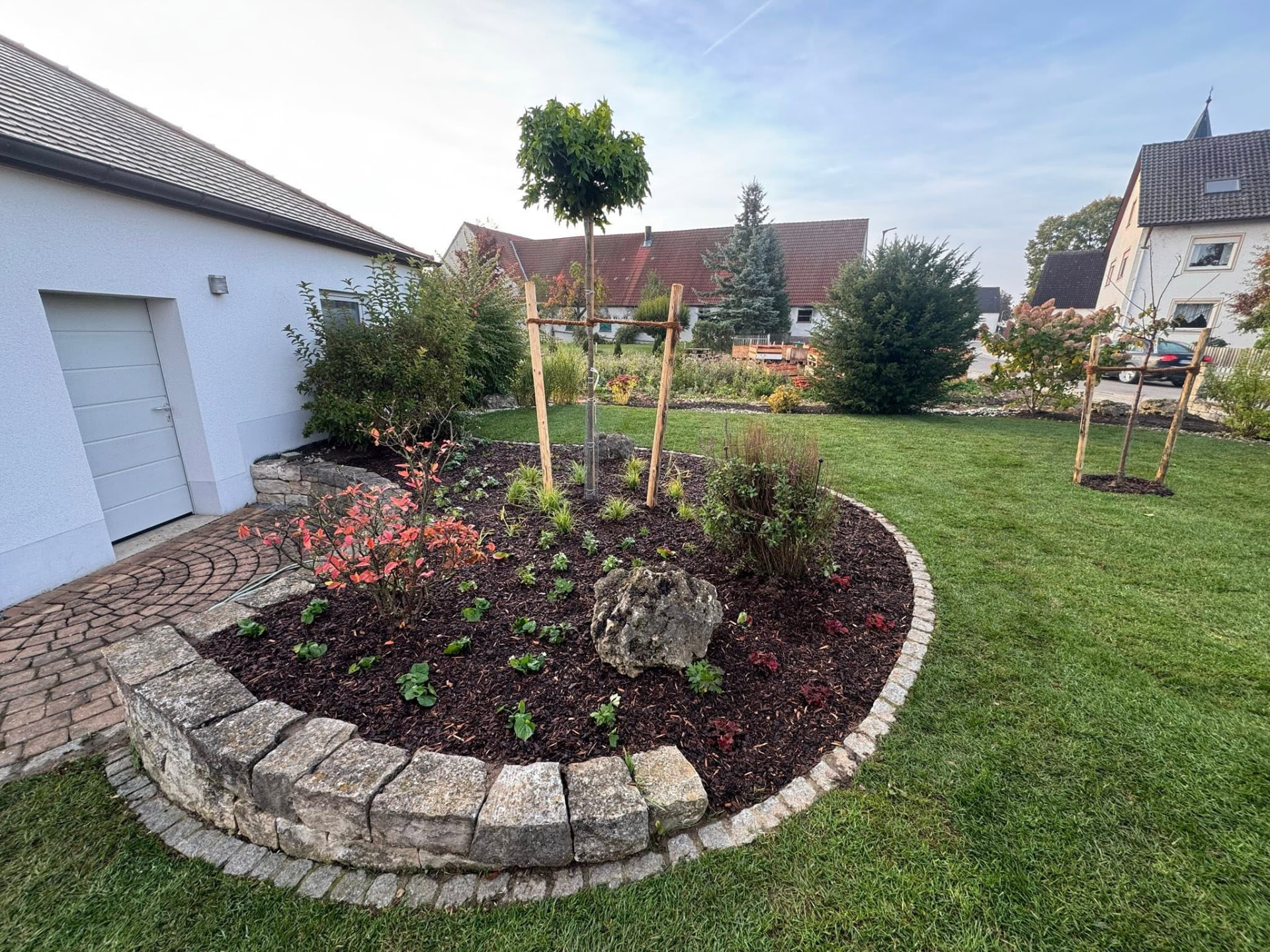 Neu angelegtes Beet mit Baum, Natursteinumrandung und gepflegtem Rasen in einem Privatgarten